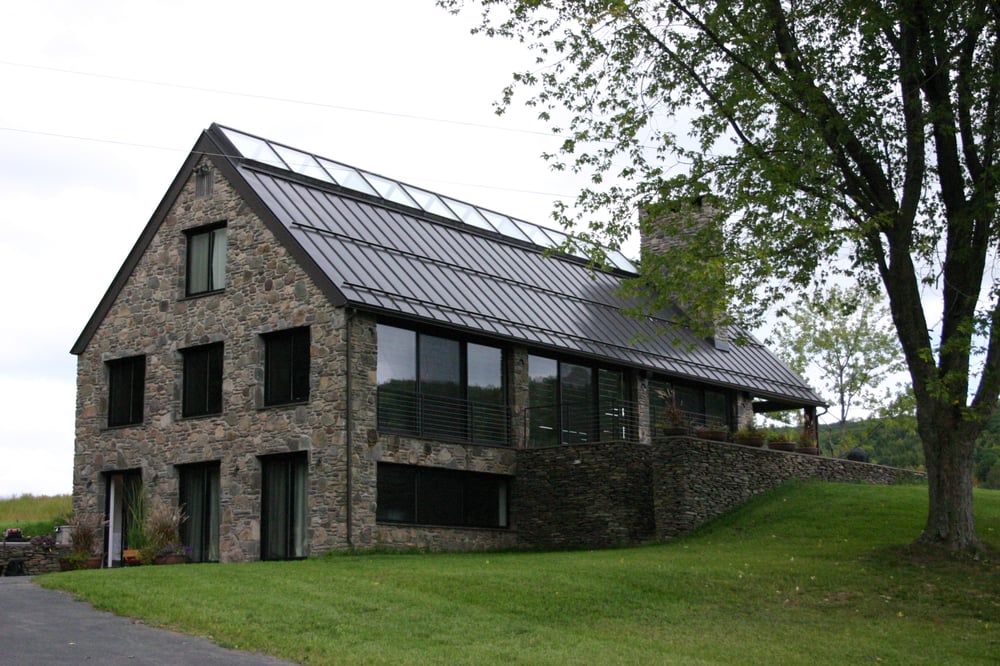 Stone house with a tall chimney, metal roof and covered patio